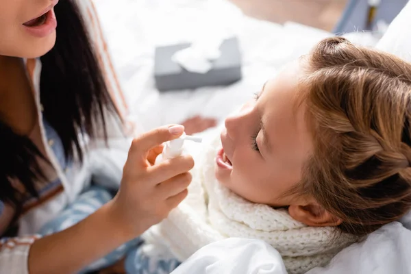 Sick girl with open mouth and closed eyes near mother applying throat spray — Stock Photo