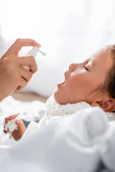 Vue latérale de la mère appliquant un spray sur le mal de gorge de la fille malade — Photo de stock