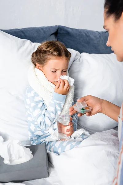 Femme donnant des médicaments à un enfant malade tenant un verre d'eau et éternuant dans une serviette en papier — Photo de stock