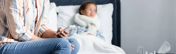 Mujer charlando en el teléfono móvil cerca de niño enfermo acostado en la cama sobre fondo borroso, pancarta - foto de stock
