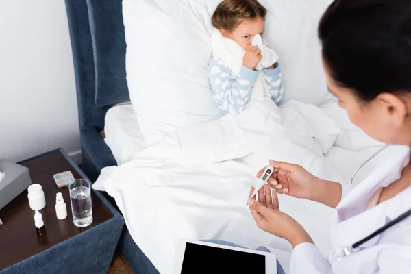 Malade fille essuyant nez avec serviette en papier près médecin regardant thermomètre — Photo de stock