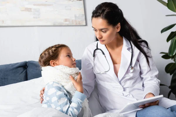 Niño enfermo tocando dolor de garganta cerca del médico sosteniendo tableta digital - foto de stock