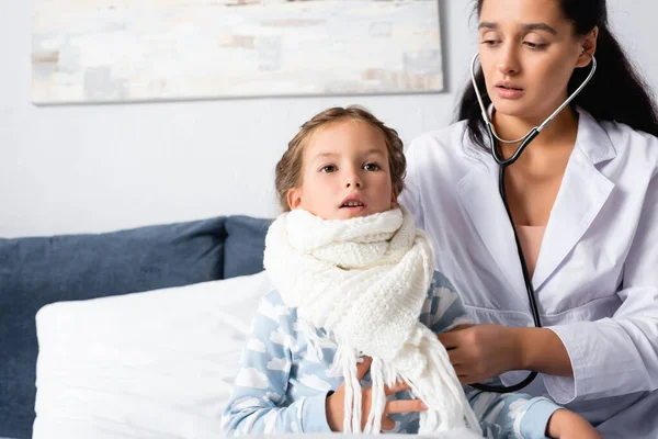 Pédiatre examen fille, enveloppé dans une écharpe chaude, avec stéthoscope — Photo de stock