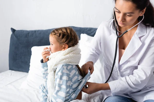 Pediatra examinando al niño enfermo, limpiando la nariz con servilleta de papel, con estetoscopio - foto de stock