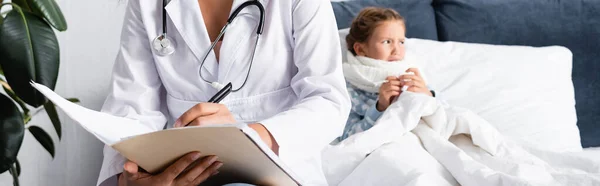 Doctor writing prescription near sick, upset child lying in bed, banner — Stock Photo
