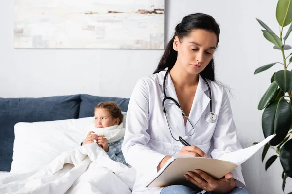 Расстроенный, больной ребенок лежит в постели рядом с врачом выписывает рецепт — стоковое фото