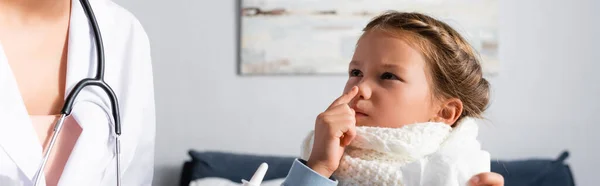 Enfant malade pointant vers le nez près du pédiatre à la maison, bannière — Photo de stock