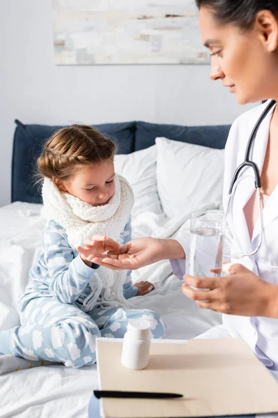 Médico dando pílula para menina doente em cachecol quente e pijama — Fotografia de Stock