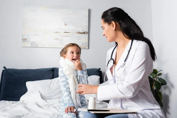 Doctor giving glass of water to diseased child taking pill — Stock Photo