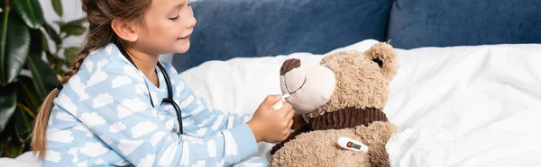 Niño jugando mientras cura oso de peluche con aerosol de garganta, pancarta - foto de stock