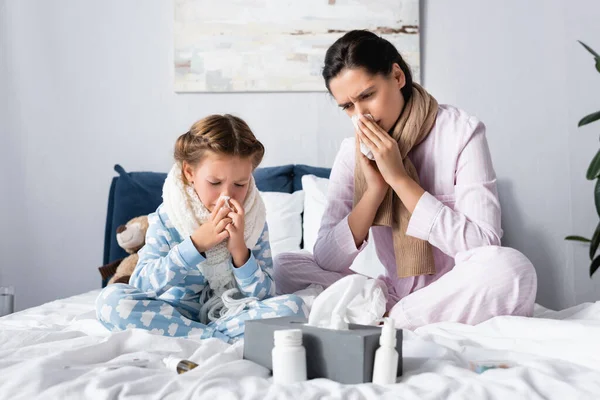 Sick mother and daughter wiping noses with paper napkins while sitting in bed — Stock Photo