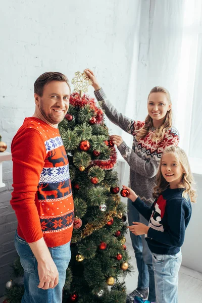 Chica feliz decorando árbol de Navidad con padres alegres en casa - foto de stock