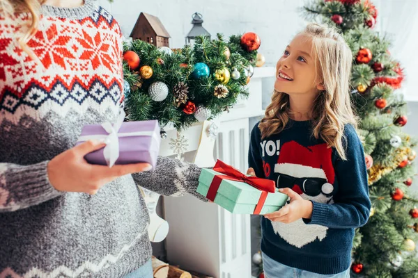 Chica feliz mirando a la madre con regalos en Navidad - foto de stock