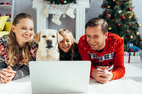 Pais alegres assistindo filme no laptop perto da filha e do cão no Natal — Fotografia de Stock