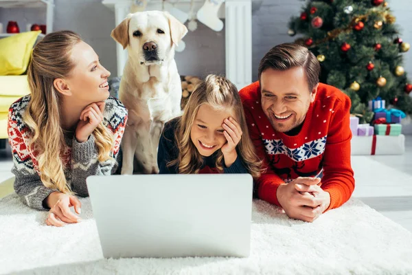 Heureux famille rire tout en regardant film sur ordinateur portable près de chien sur noël — Photo de stock