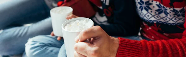 Cropped view of man and woman holding cocoa with marshmallows in mugs, banner — Stock Photo