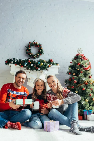 Happy family holding cups and gifts near christmas tree — Stock Photo