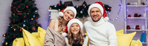 Happy family in santa hats looking at camera in decorated living room, banner — Stock Photo