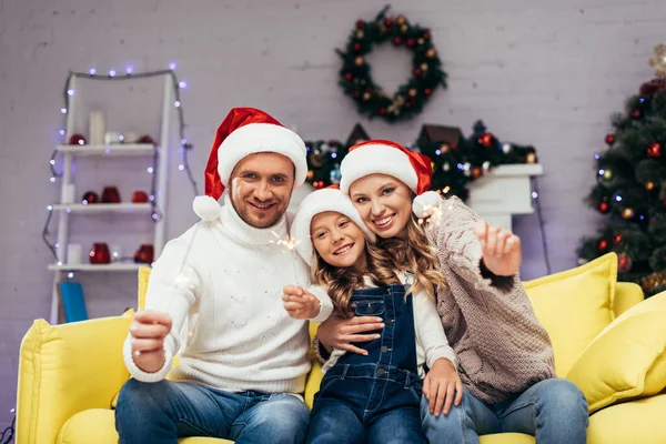 Щаслива сім'я в капелюхах Санти тримає блискітки в декорованій вітальні на Різдво — стокове фото