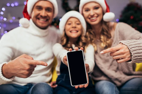 Smartphone con pantalla en blanco y familia borrosa y feliz en segundo plano - foto de stock