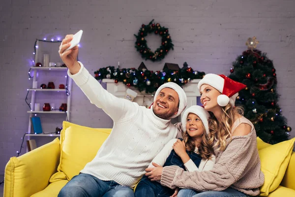 Glückliche Familie in Weihnachtsmannmützen macht Selfie im dekorierten Wohnzimmer — Stockfoto