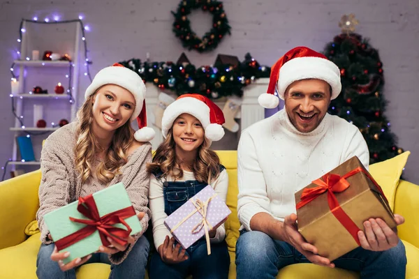 Freudige Familie in Weihnachtsmützen mit Geschenken im geschmückten Wohnzimmer an Weihnachten — Stockfoto