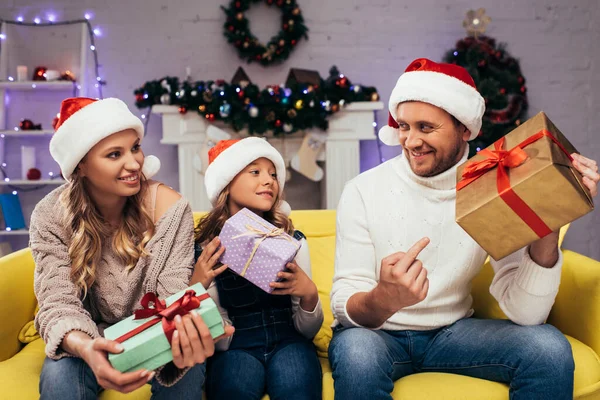 Familia feliz en sombreros de santa celebración de regalos en la sala de estar decorada en Navidad - foto de stock