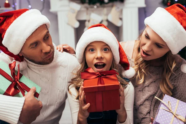 Шокированный ребенок держит Рождество подарок рядом с родителями — стоковое фото
