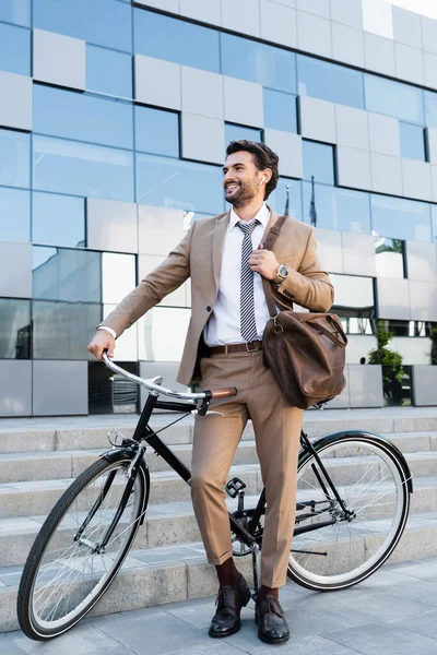 Longitud completa de hombre de negocios alegre en auriculares inalámbricos de pie cerca de la bicicleta - foto de stock
