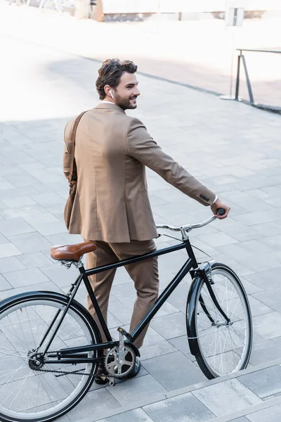 Piena lunghezza di felice uomo d'affari in auricolari wireless in piedi vicino alla bicicletta — Foto stock