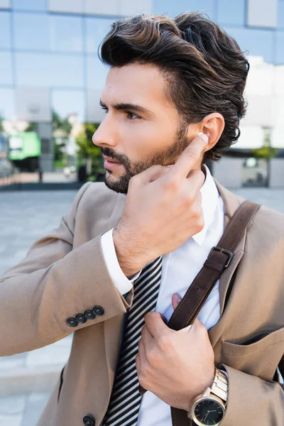 Bearded businessman adjusting wireless earphones outside — Stock Photo