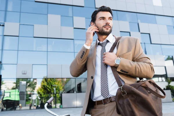 Bearded businessman adjusting wireless earphones while standing near building — Stock Photo