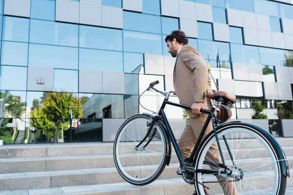 Full length of businessman in wireless earphones walking on stairs with bicycle — Stock Photo