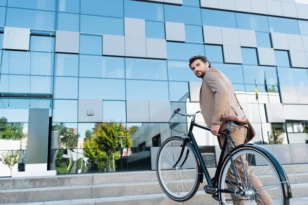 Homem de negócios barbudo em fones de ouvido sem fio andando em escadas com bicicleta — Fotografia de Stock