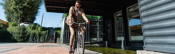 Full length of businessman in wireless earphones riding bicycle, banner — Stock Photo