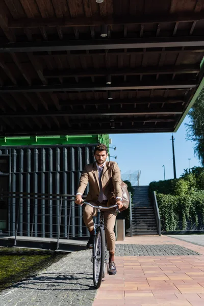 В полный рост бизнесмен в беспроводных наушниках ездит на велосипеде — стоковое фото