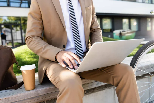 Vista cortada de homem de negócios usando laptop perto de copo de papel — Fotografia de Stock