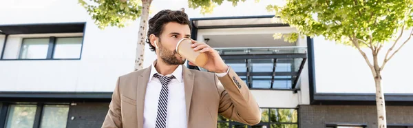 Homem de negócios em fones de ouvido sem fio e terno beber café para ir, banner — Fotografia de Stock