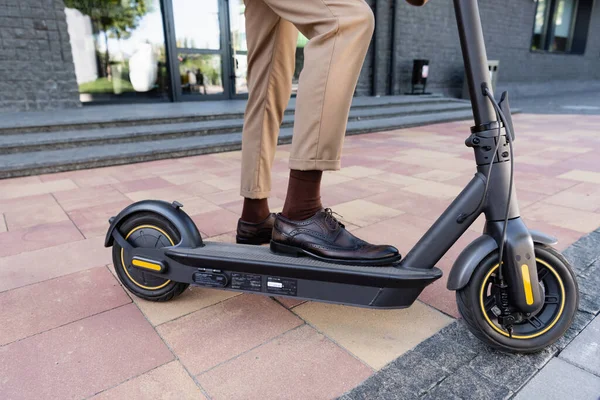 Vista parcial del hombre de negocios sosteniendo bolsa de cuero mientras está de pie cerca de e-scooter y el edificio - foto de stock