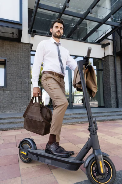 Full length of businessman in formal wear standing near e-scooter with leather bag — Stock Photo