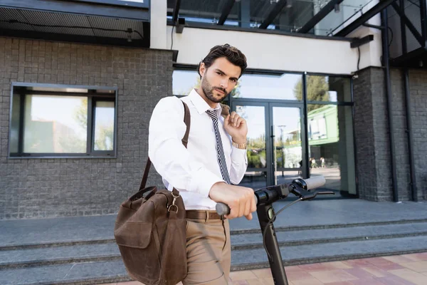 Hombre de negocios en traje de pie cerca de e-scooter con bolsa de cuero — Stock Photo