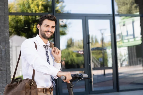 Щасливий бізнесмен в офіційному одязі, що стоїть біля електронного скутера зі шкіряною сумкою — стокове фото