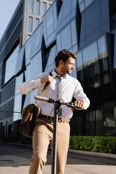 Homem de negócios em desgaste formal de pé perto de scooter elétrico e ajustando saco de couro — Fotografia de Stock
