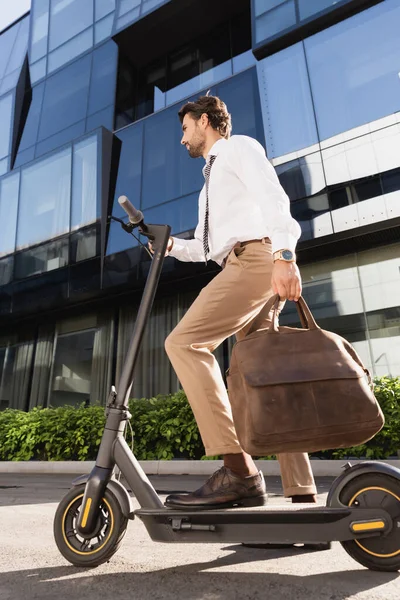 Full length of businessman in suit with leather bag riding electric scooter — Stock Photo