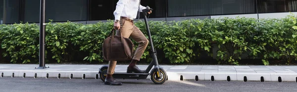 Vista recortada de hombre de negocios en el desgaste formal montar scooter eléctrico y bolsa de sujeción, pancarta - foto de stock