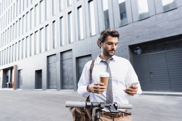 Homem de negócios barbudo em uso formal segurando copo de papel e usando smartphone perto de e-scooter — Stock Photo