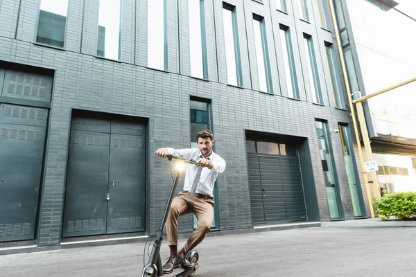 Piena lunghezza di uomo d'affari in abbigliamento formale guida scooter elettrico vicino edificio — Foto stock