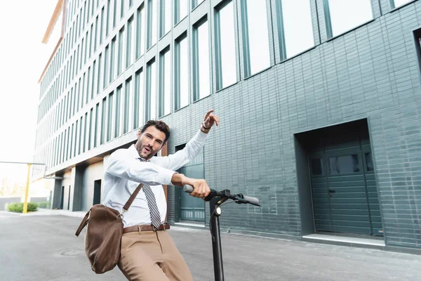 Empresário animado no desgaste formal equitação scooter elétrico perto do edifício — Fotografia de Stock