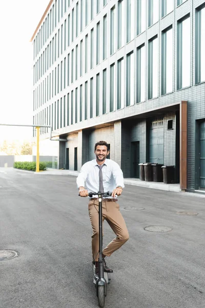 Comprimento total de empresário feliz no desgaste formal equitação scooter elétrico perto do edifício — Fotografia de Stock