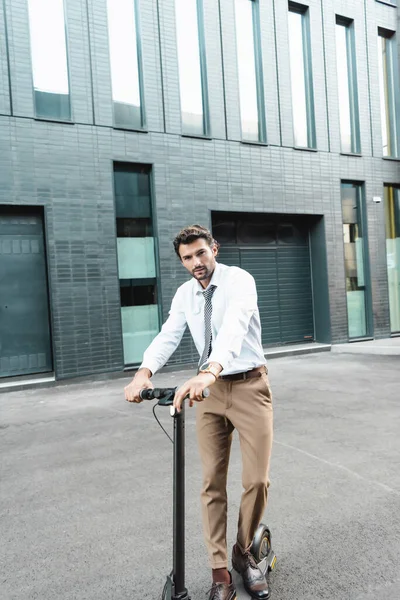 Повна довжина бізнесмена в офіційному одязі верхи сучасний електричний скутер біля будівлі — стокове фото